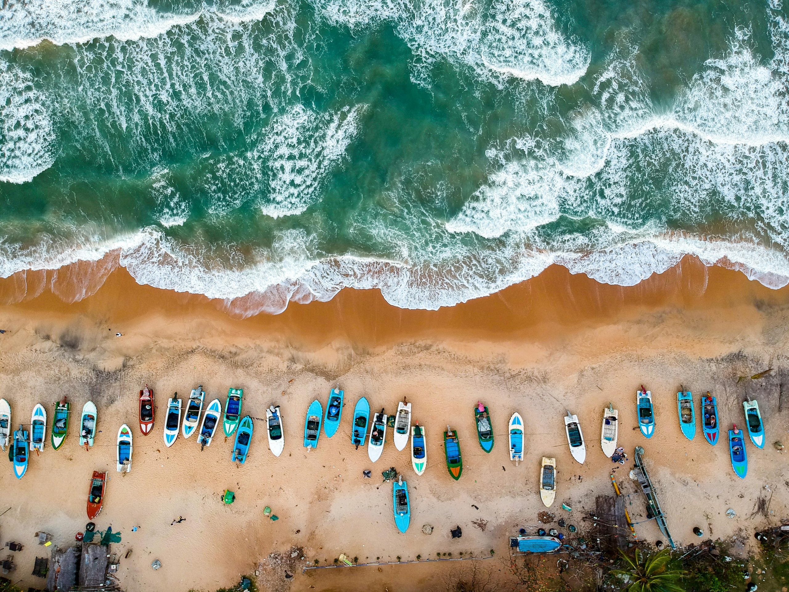 Stunning aerial shot of vibrant boats lined on sandy shores of Arugam Bay, Sri Lanka.